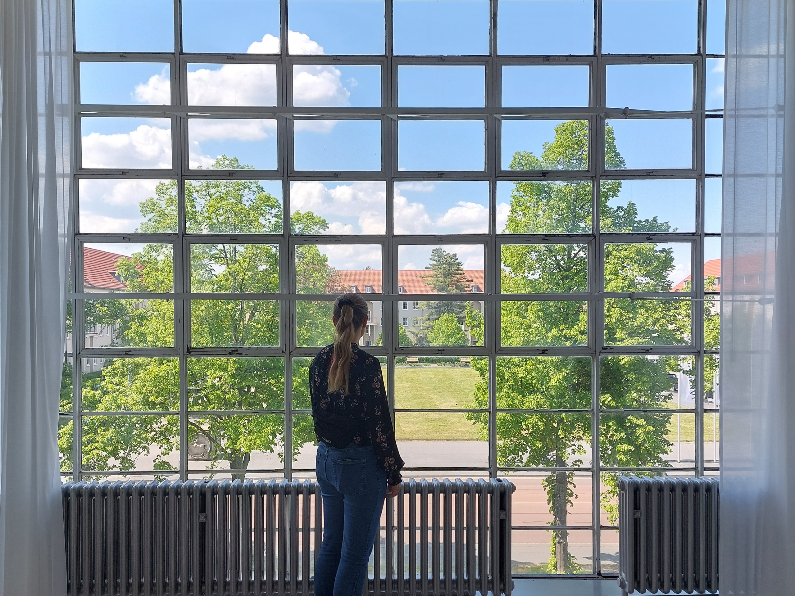 Eine junge Frau schaut aus einer Fensterfront des Bauhaus-Gebäudes in Dessau.